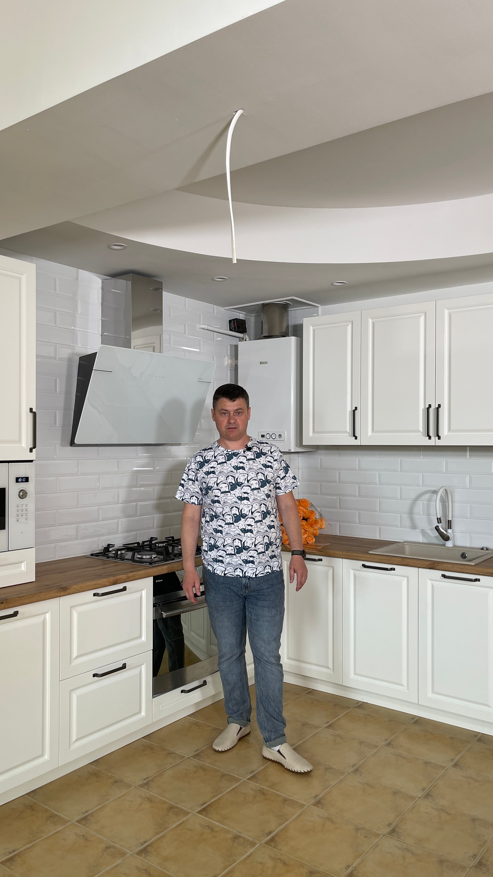 Мужчина стоит на фоне белой угловой кухни с фартуком кабанчик