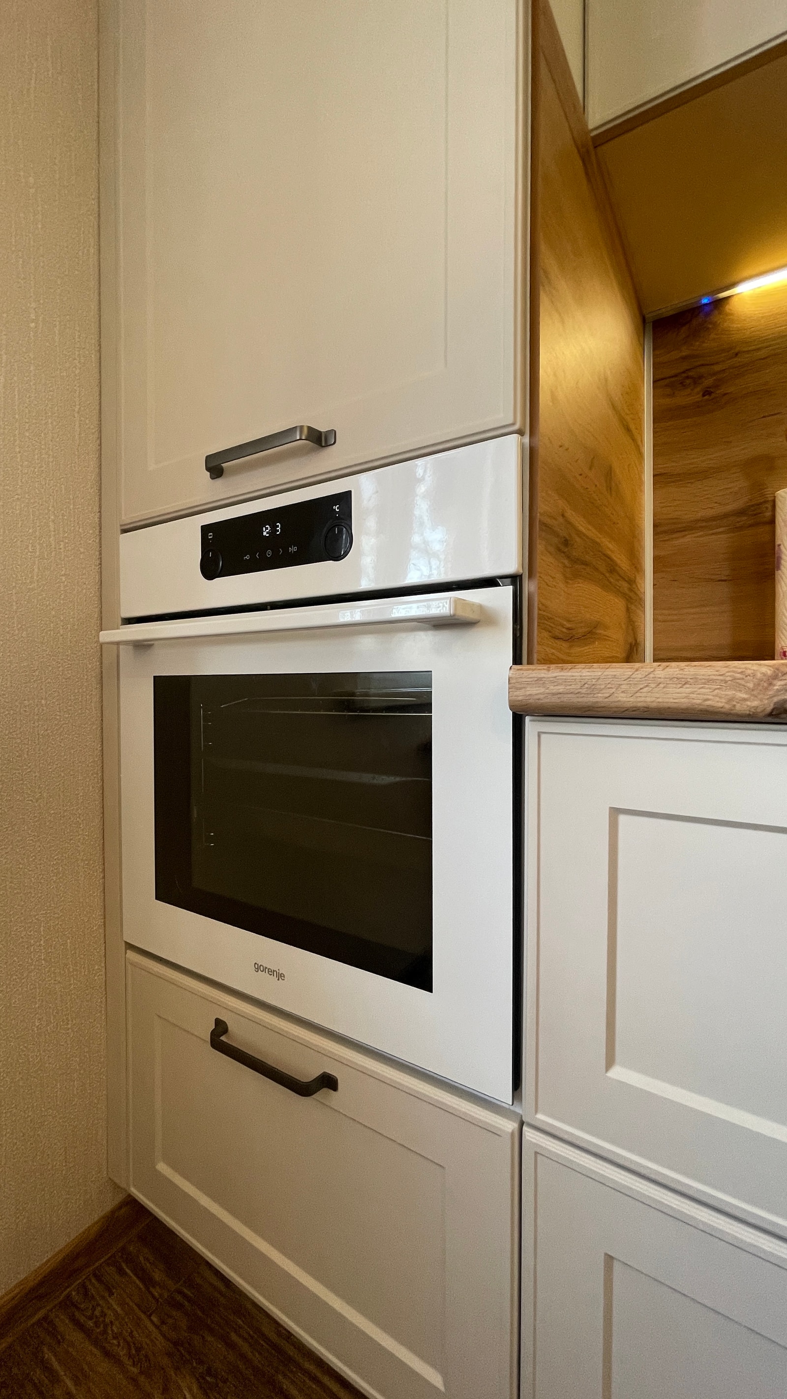 Колонна со встроенной духовкой Gorenje в светлой неоклассической кухне с дубовой нишей