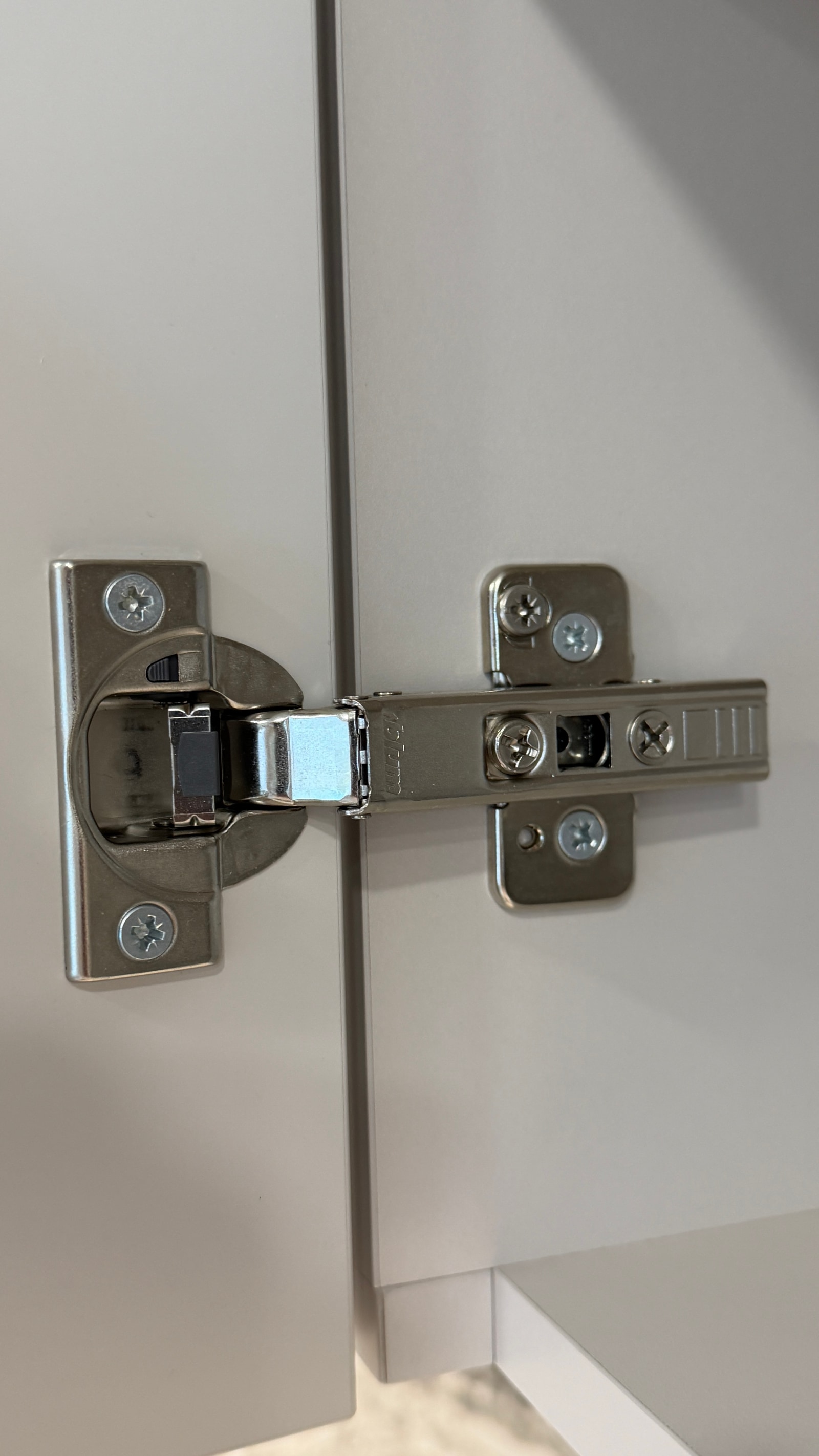 Крупный план мебельной петли Blum на белом фасаде шкафа — монтаж, хромированная фурнитура