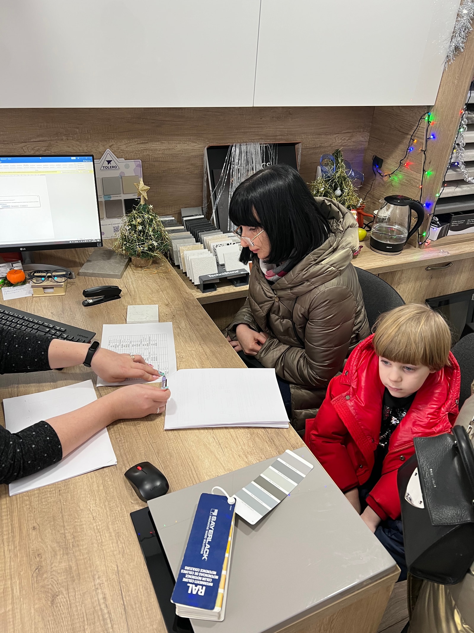 Женщина-клиент с ребёнком подписывает документы у менеджера в офисе шоурума, на столе каталог RAL