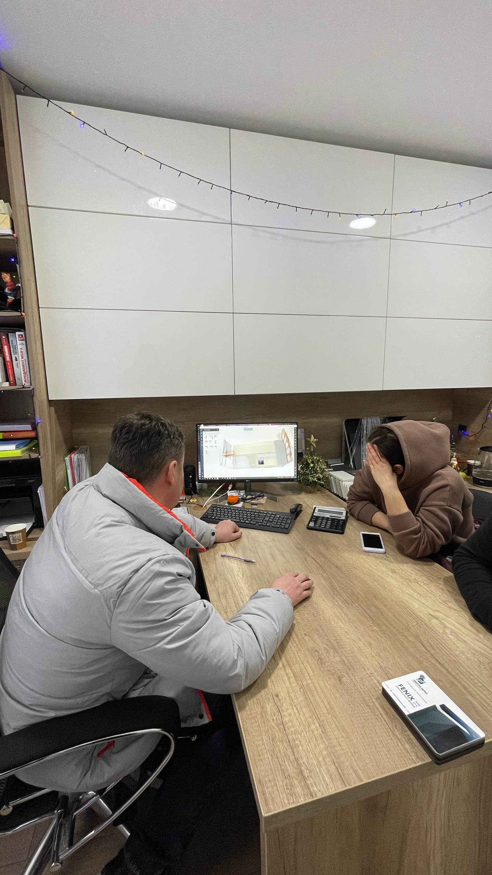 Двое сотрудников за рабочим столом в офисе шоурума обсуждают проект кухни на мониторе, новогодний декор