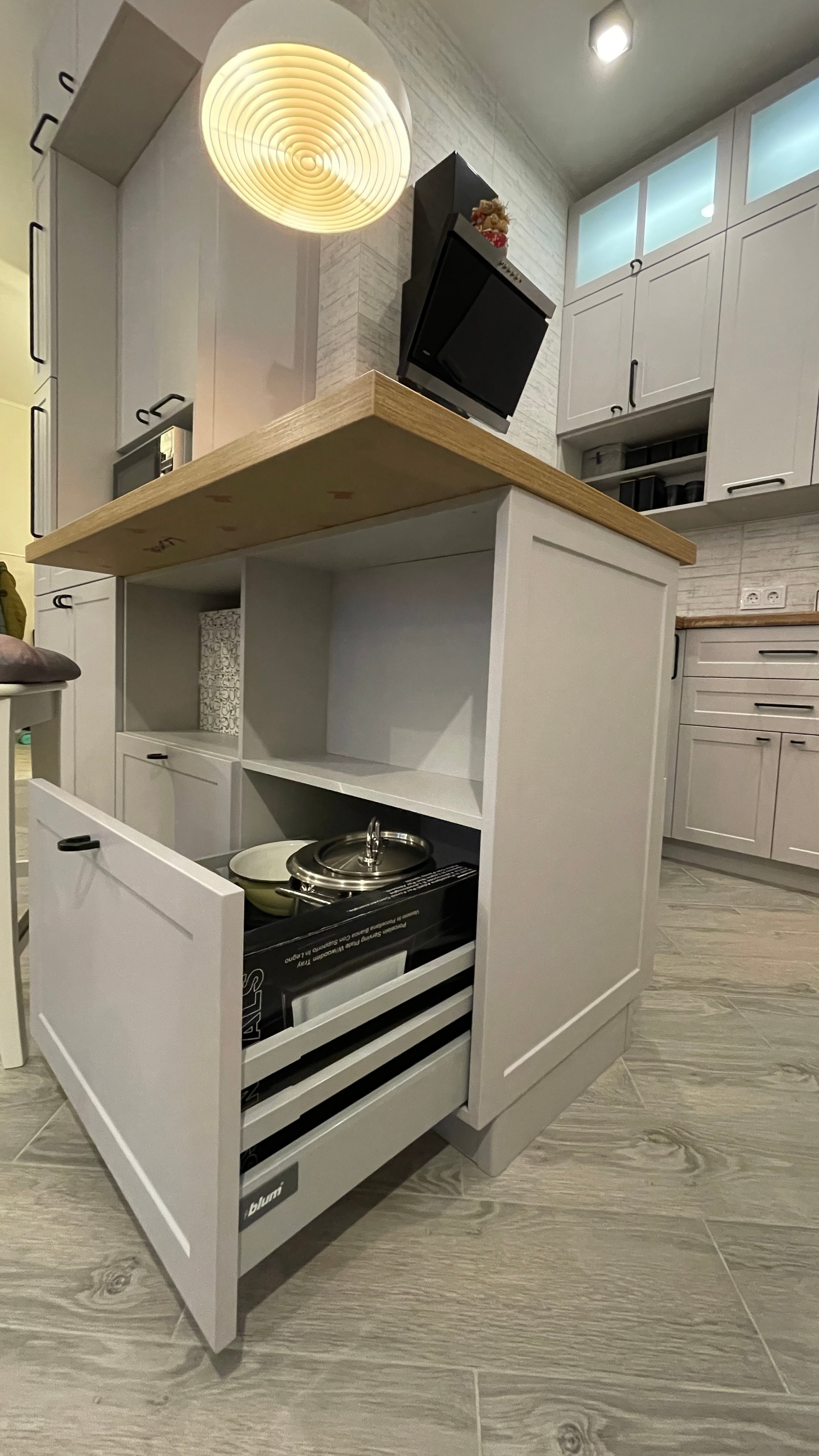 Крупный план открытого выдвижного ящика Blum в белом кухонном острове с деревянной столешницей и посудой внутри