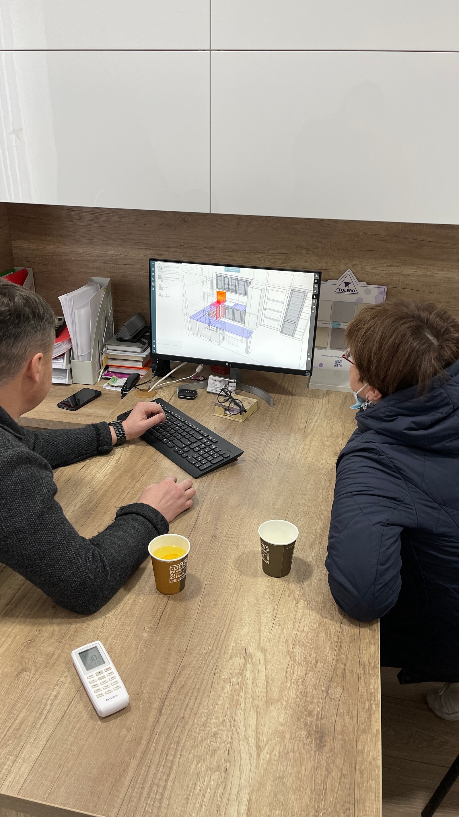 Сотрудник и клиент рядом смотрят на 3D-визуализацию кухни на мониторе, крупный план экрана