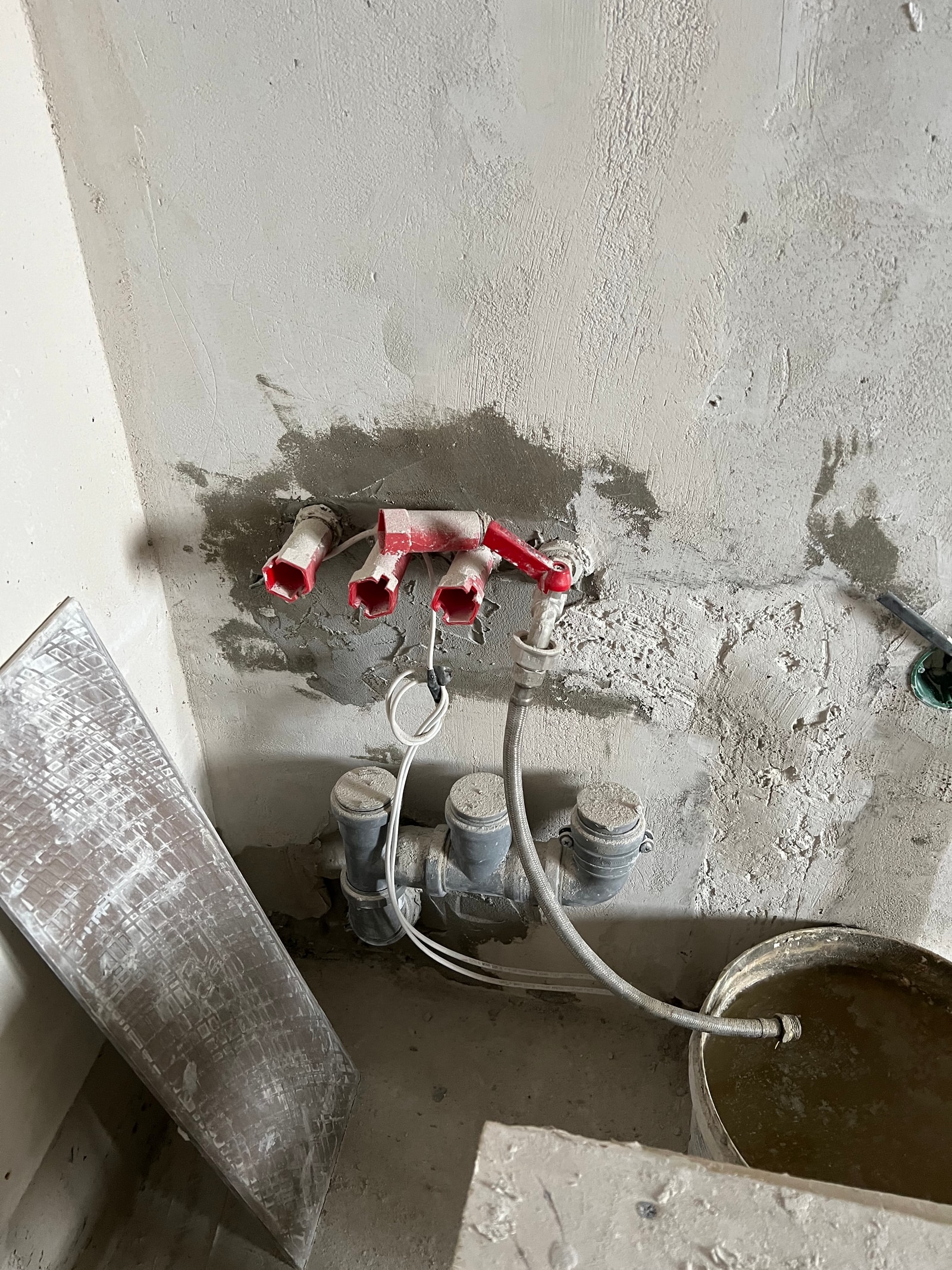 Крупный план угла стены с выведенными трубами водоснабжения и электрическими подрозетниками на стадии ремонта