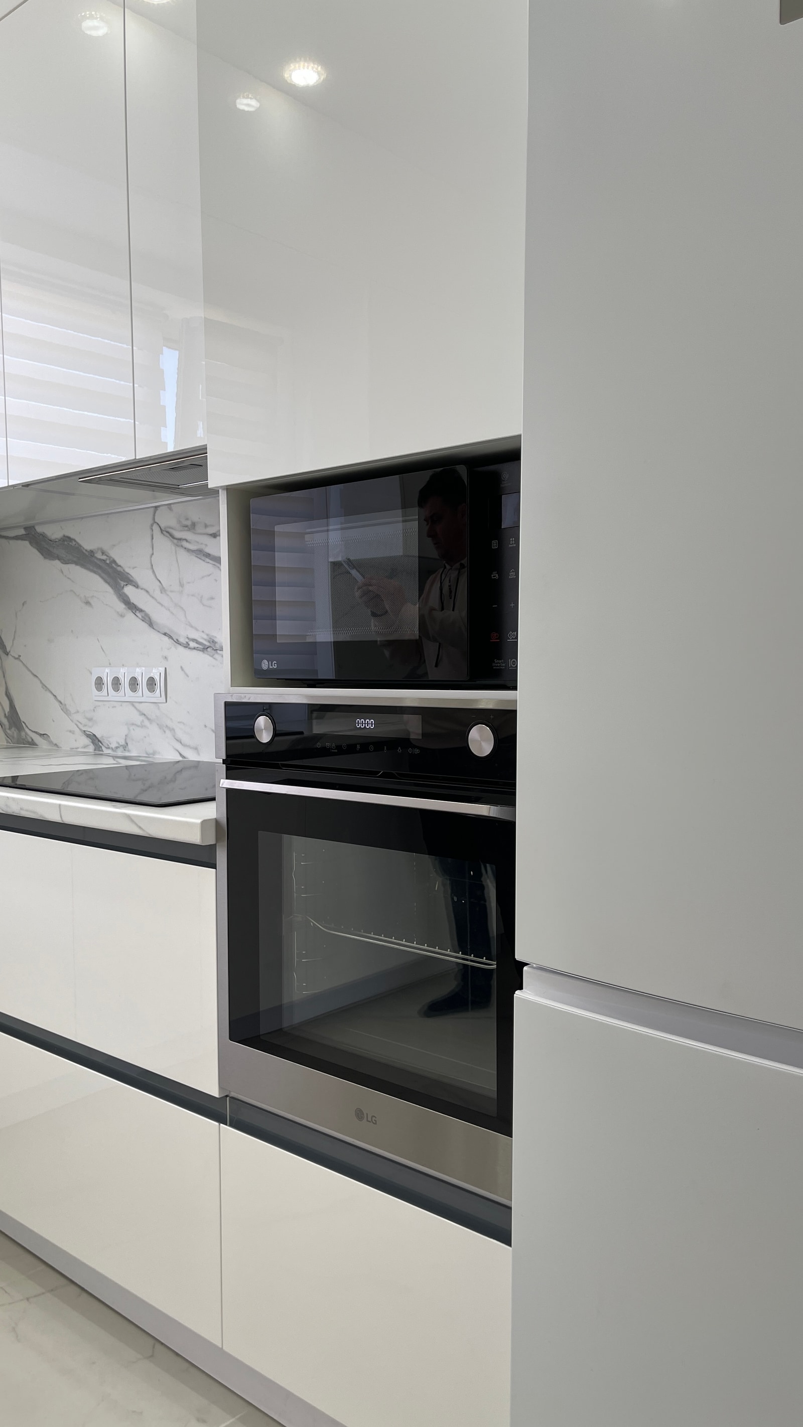 Пенал с встроенными микроволновкой и духовкой LG в белой глянцевой кухне, мраморный фартук и варочная панель слева