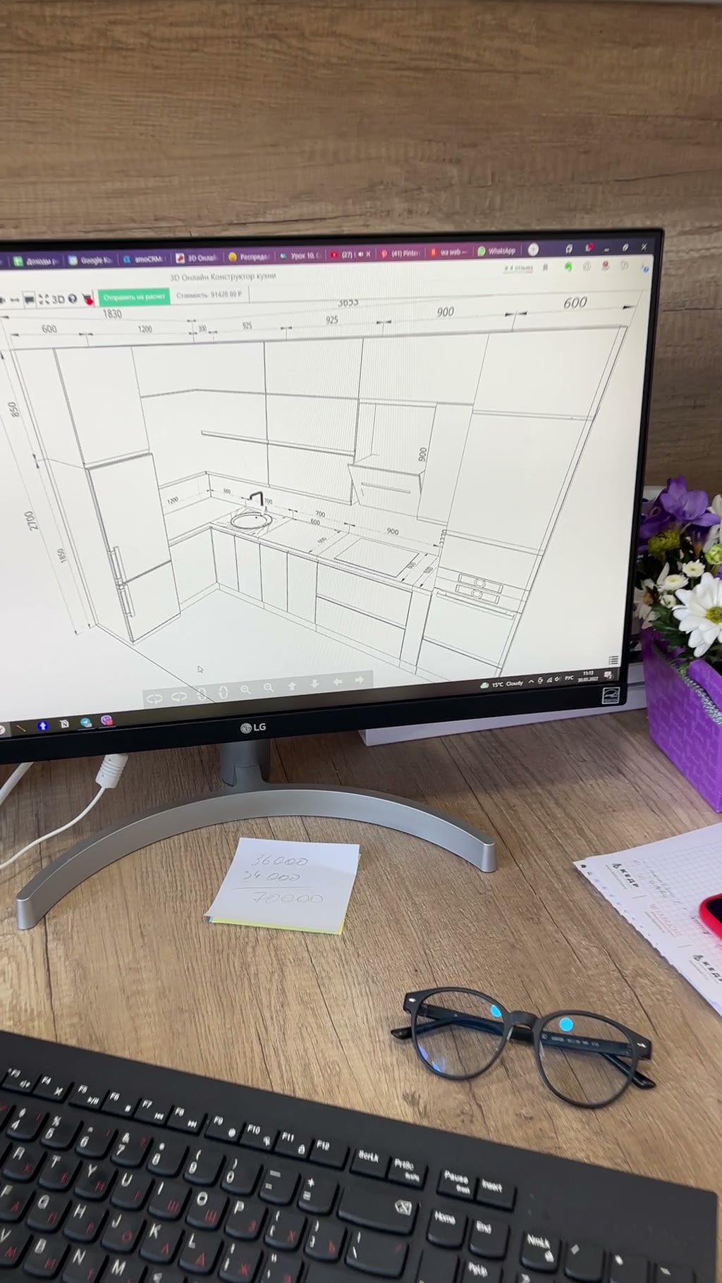 Монитор LG с 3D-проектом угловой кухни в онлайн-конструкторе, на столе стикер с ценами, очки и букет ромашек